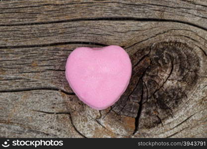 Close up of a single pink heart shaped candy on rustic wood. Valentines day concept.