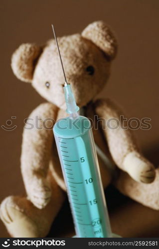 Close-up of a syringe in front of a teddy bear