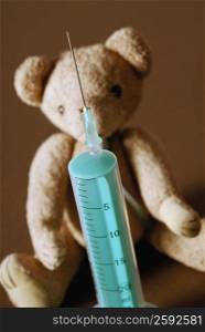 Close-up of a syringe in front of a teddy bear