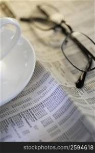 Close-up of a tea cup and eyeglasses on a newspaper