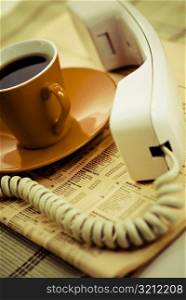 Close-up of a tea cup with a telephone receiver on the financial newspaper