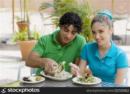 Close-up of a teenage girl and a young man eating salad and a wrap in a restaurant