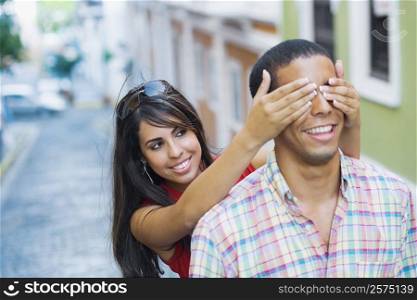 Close-up of a teenage girl covering a young man&acute;s eyes from behind