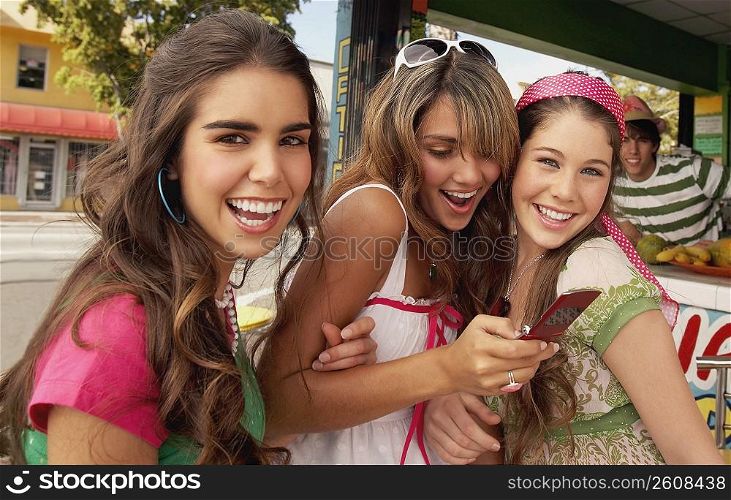 Close-up of a teenage girl holding a mobile phone and standing at the juice bar with her friends