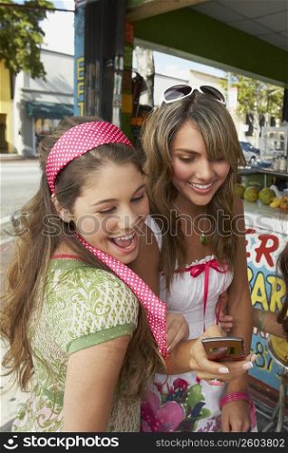 Close-up of a teenage girl holding a mobile phone and standing with her friend