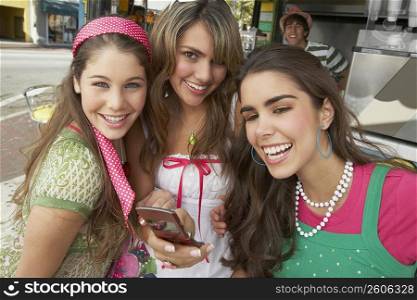 Close-up of a teenage girl holding a mobile phone and standing with her friends