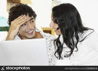 Close-up of a teenage girl looking at a young man in front of a laptop
