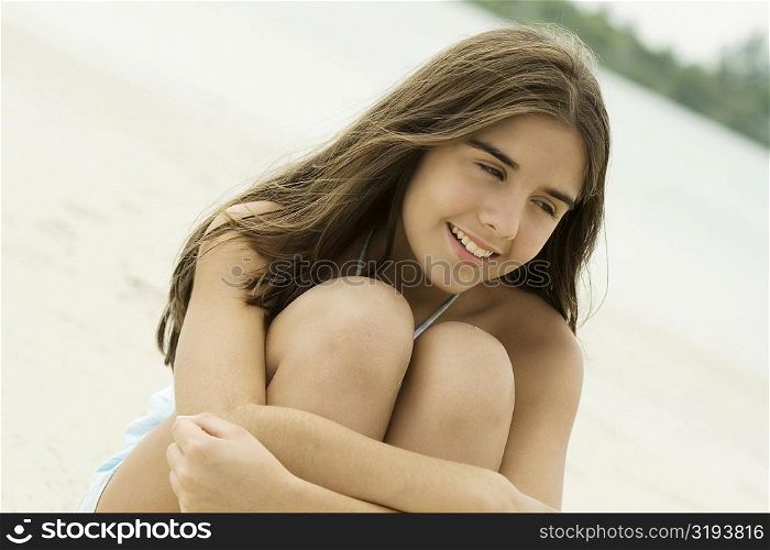 Close-up of a teenage girl sitting on the beach smiling