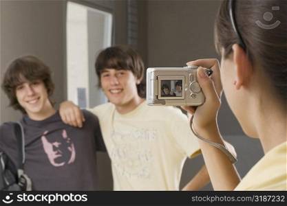 Close-up of a teenage girl taking a photograph of her two friends with a digital camera