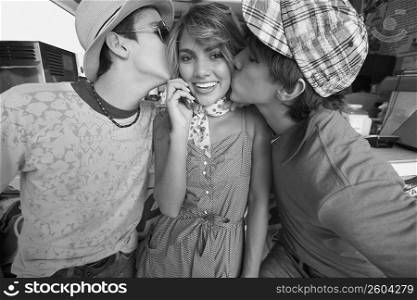 Close-up of a teenage girl talking on a mobile phone with her two boyfriends kissing her