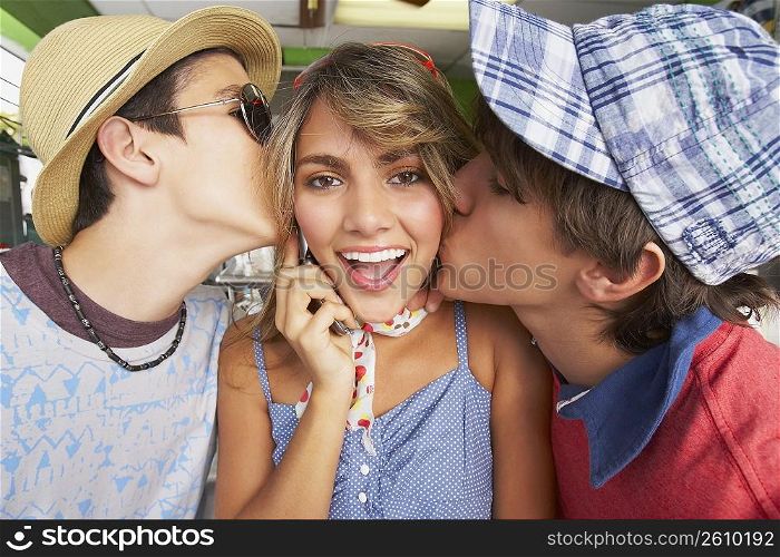 Close-up of a teenage girl talking on a mobile phone with her two boyfriends kissing her