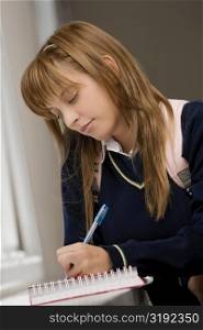 Close-up of a teenage girl writing in a spiral notebook