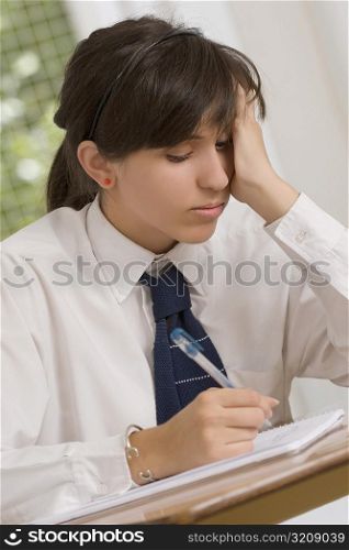 Close-up of a teenage girl writing in a spiral notebook with her head in her hand