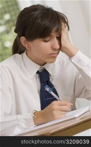 Close-up of a teenage girl writing in a spiral notebook with her head in her hand