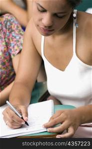 Close-up of a teenage girl writing with a pen in a notepad