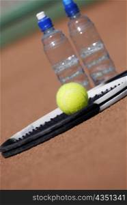 Close-up of a tennis racket and a tennis ball with two water bottles