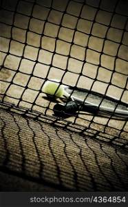 Close-up of a tennis racket and tennis ball viewed through the net in a court