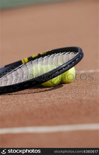 Close-up of a tennis racket and three tennis balls on a tennis court