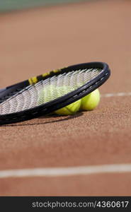 Close-up of a tennis racket and three tennis balls on a tennis court