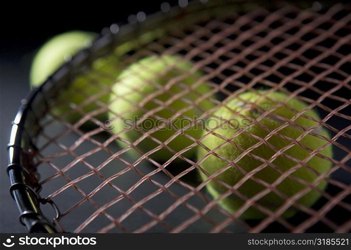 Close-up of a tennis racket with three tennis balls
