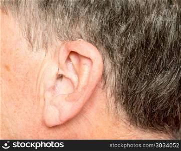 Close up of a tiny modern hearing aid behind ear. Macro close up of tiny modern hearing aid placed behind the ear of senior adult man. Close up of a tiny modern hearing aid behind ear