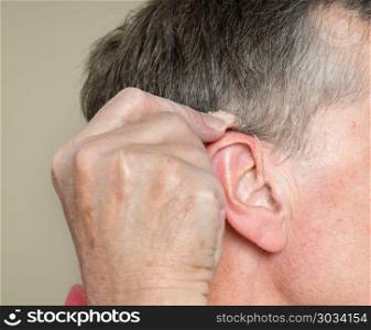 Close up of a tiny modern hearing aid behind ear. Macro close up of tiny modern hearing aid placed behind the ear of senior adult man. Close up of a tiny modern hearing aid behind ear