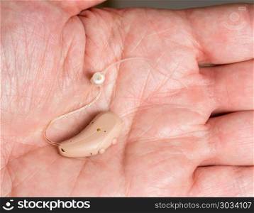 Close up of a tiny modern hearing aid in palm. Macro close up of tiny modern hearing aid in the palm of senior adult man. Close up of a tiny modern hearing aid in palm