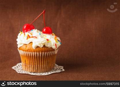 Close-up of a tiny tart with cherry on top on a brown background. Tasty cupcake with cherry