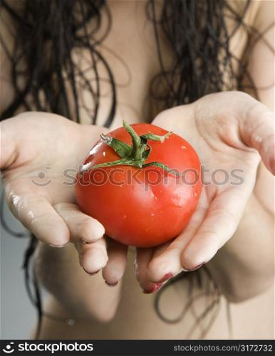 Close up of a topless Caucasian woman holding tomatoes.
