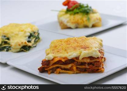 Close-up of a traditional lasagna made with minced beef bolognese sauce topped with basil leafs served on a white plate