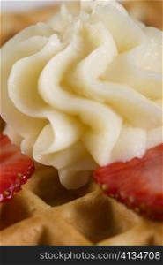 Close-up of a waffle with strawberry slice and whipped cream on it