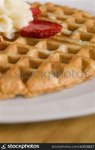 Close-up of a waffle with whipped cream and strawberry slice on it
