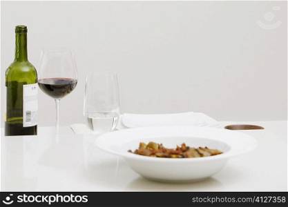 Close-up of a wine bottle with a glass of red wine and a bowl on a dining table