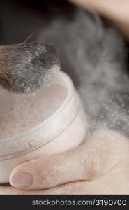 Close-up of a woman&acute;s hand holding a pot of face powder and a make-up brush