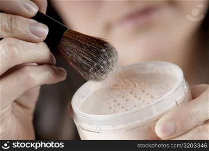 Close-up of a woman&acute;s hand holding a pot of face powder and a make-up brush