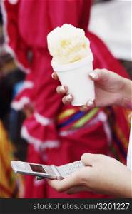 Close-up of a woman&acute;s hands holding an ice-cream and using a mobile phone