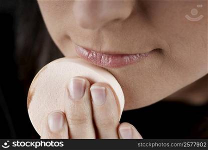 Close-up of a woman applying face powder on her chin with a powder puff