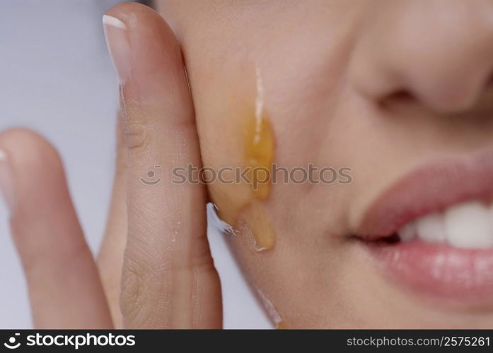 Close-up of a woman applying honey on her cheek