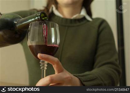 Close-up of a woman in a green jacket alone pouring a glass of red wine. Close-up view of a lonely woman pouring herself a glass of red wine