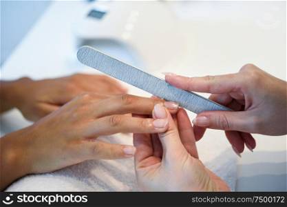 Close-up of a woman in a nail salon receiving a manicure by a beautician with. Beautician file nails to a customer.. Woman in a nails salon receiving a manicure with nail file