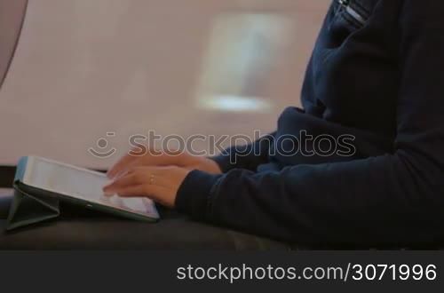 Close-up of a woman sitting by window in the train, holding touch pad on the lap and typing message. Easy communication on the way