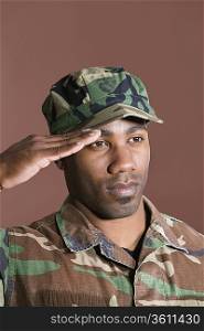 Close-up of a young African American US Marine Corps soldier saluting over brown background