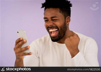 Close-up of a young afro man celebrating victory while looking at his mobile phone against isolated background. Success concept.