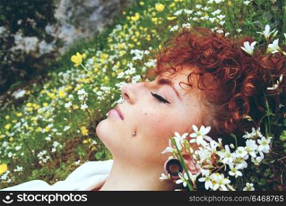 Close up of a young and redhead woman sleeping in a field of flowers