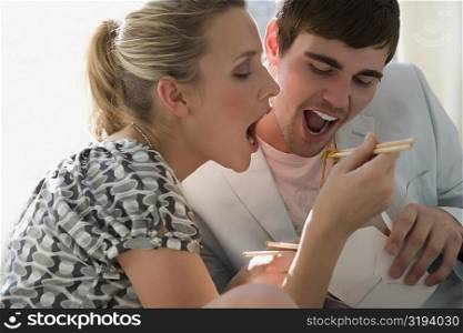 Close-up of a young couple eating noodles from a carton