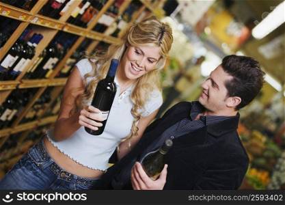 Close-up of a young couple holding wine bottles in a liquor store