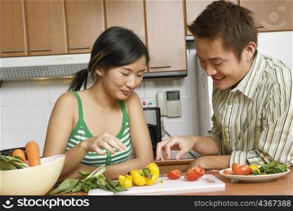 Close-up of a young couple looking at sliced vegetables on a cutting board at a kitchen counter