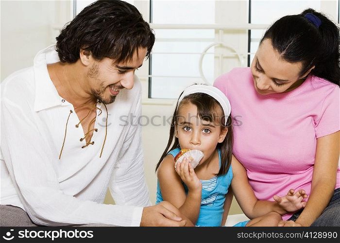 Close-up of a young couple looking at their daughter eating a pastry