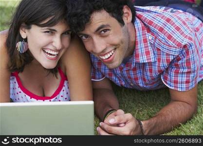 Close-up of a young couple lying in a lawn in front of a laptop
