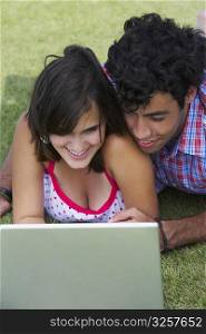 Close-up of a young couple lying in a lawn in front of a laptop